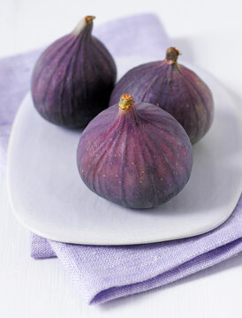 Three fresh purple figs sit on a white plate indoors