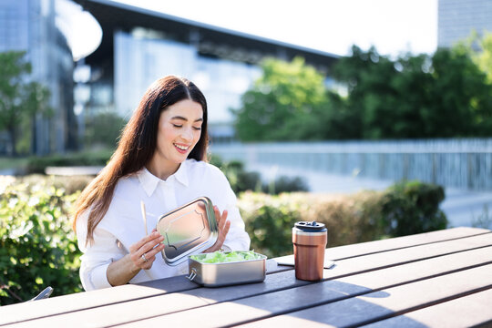 Businesswoman opens reusable lunch box with salad outdoors