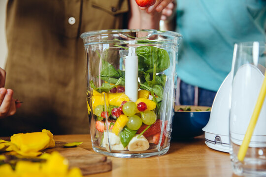 Close-up of mother and children putting fruit into a smoothie blender