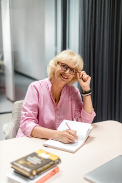 Smiling businesswoman writes a note at a desk
