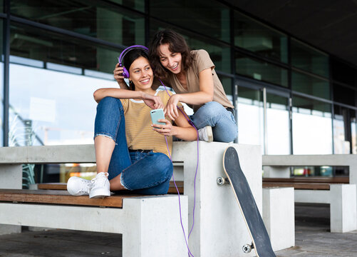 Happy woman shares music on a smartphone with a friend outdoors