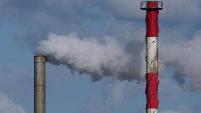 Industrial factory chimney stack emitting white smoke plumes into clear blue sky.