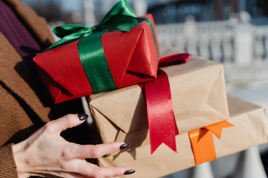 Woman holds wrapped gift stack outdoors during winter shopping