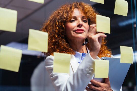 Businesswoman writes on a note on a glass wall at the office