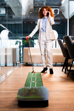Businesswoman plays golf and talks on smartphone in office