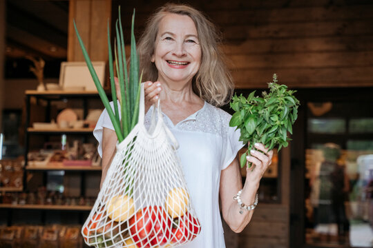Smiling senior woman holds a reusable bag with fresh food
