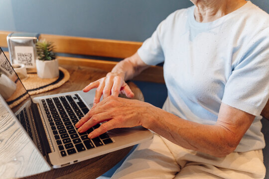 Elderly woman types on a laptop at a cafe table indoors