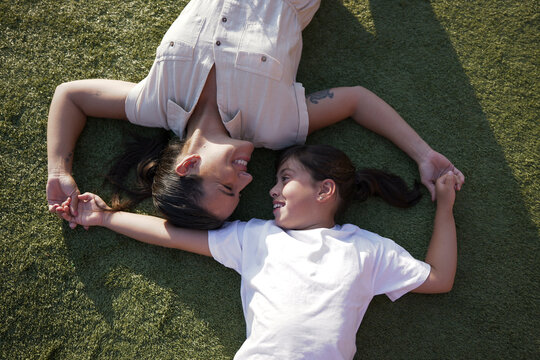 Mother and daughter hold hands lying on the grass in summer