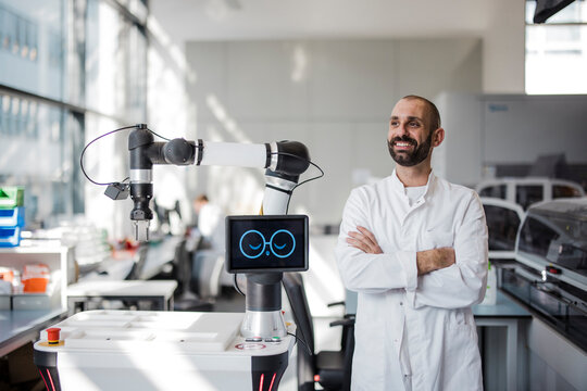 Smiling scientist stands next to a robot in a modern laboratory