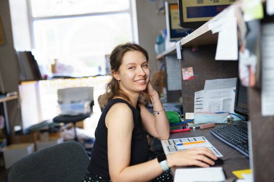 Smiling young woman working at computer in a print shop office