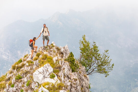 Italy, Massa, man helping woman to climb on top of a peak in the Alpi Apuane mountains