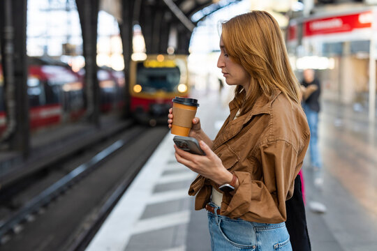 Woman waiting for train at Berlin station looking at mobile phone