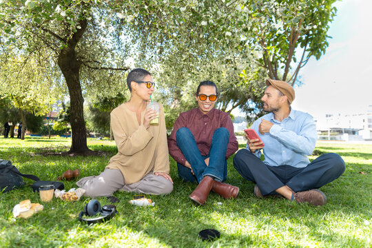 Friends sit on the grass in a park enjoying a weekend picnic