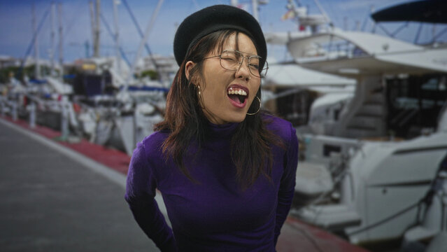 Young asian woman with open mouth and round glasses, wearing a black beret and purple turtleneck, hands clasped behind back on a street by moored yachts; joy spontaneity.