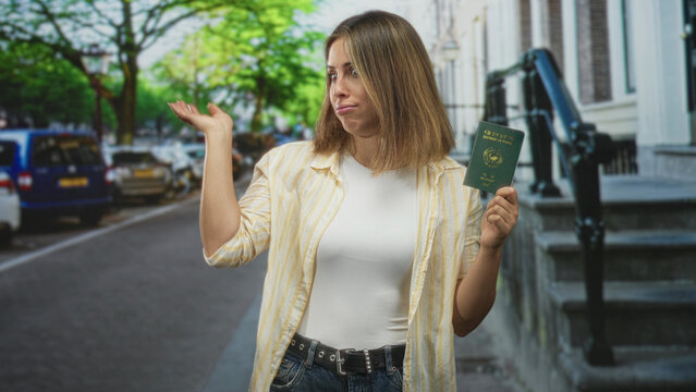 Woman holding passport in right hand waves dismissive palm on busy city street by building steps wearing casual shirt and jeans; frustration travel delay.