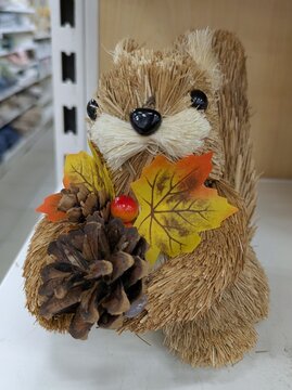 Tiempo de oto&ntilde;o. Simp&aacute;tico mu&ntilde;eco de ardilla de estilo artesanal, sujetando hojas, bayas y pi&ntilde;as de pino, de pie en el estante de un comercio	