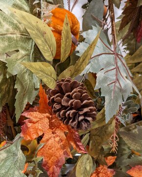 Tiempo de oto&ntilde;o. Vista de cerca de un arreglo decorativo de tem&aacute;tica oto&ntilde;al compuesto por una pi&ntilde;a de pino natural y una calabaza, ramas y diversas hojas de &aacute;rbol de materiales artificiales