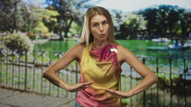 Woman with hands near abdomen performing slow breathing and gestural movement by a lakeside iron fence in a forest; serenity focus.