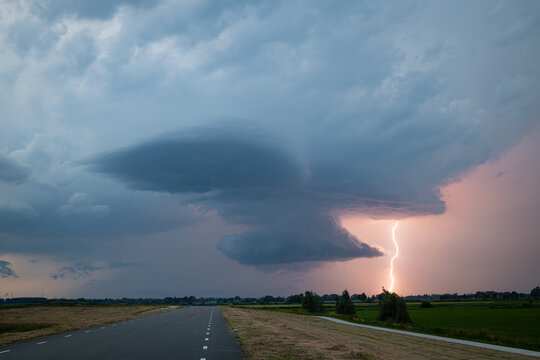 Dramatic supercell thunderstorm over rural road with lightning strike and wall cloud at dusk