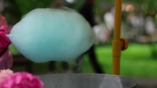 Woman making blue cotton candy with spinning machine at outdoor park. Sweet fluffy sugar cloud dessert being prepared at street food festival. Candy floss treat concept.