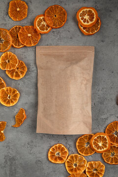 Empty brown kraft paper packaging bag and scattered dried orange wheels on a gray concrete background top view