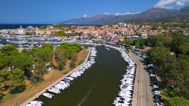 Scenic canal drone flyby with motorboat towards bridge in Saint Florent Corsica. High end luxury travel reveal of colorful town port and marina 4K Cap Corse France