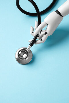 A white robotic hand holding a medical stethoscope on a light blue background. Concept of artificial intelligence in healthcare and diagnostics. Top view with copy space.