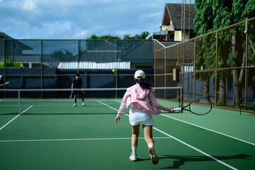 Young Asian Woman Playing Tennis on Outdoor Green Court with Friends on a Sunny Day