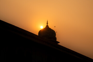 Silhouetted dome at Agra Fort beneath a glowing sun © Patrick.W