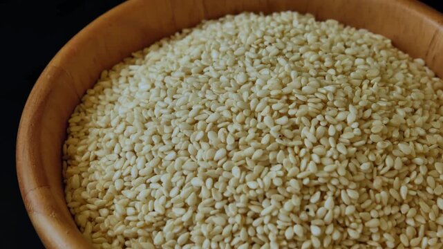 White sesame seeds arranged in a natural wooden bowl, showcasing their small size, pale color, and delicate texture.