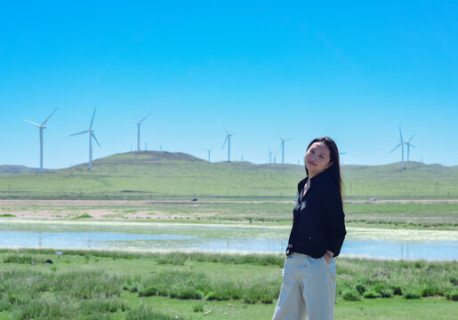 One Asian woman enjoying scenic landscape of salt lake wetland and distant wind turbines in summer in Ulan Hada Volcano Geopark, Ulanqab, Inner Mongolia, China