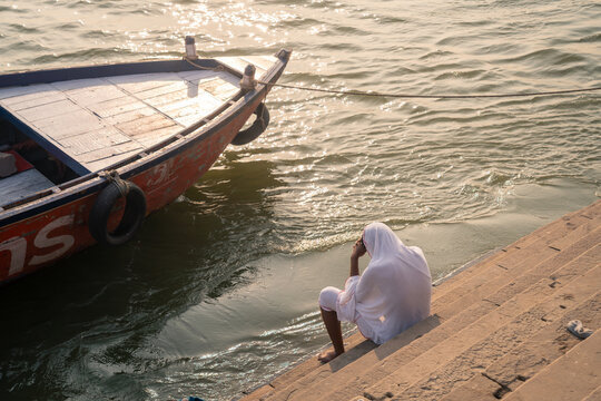 Person in white seated on Ganges steps beside a boat