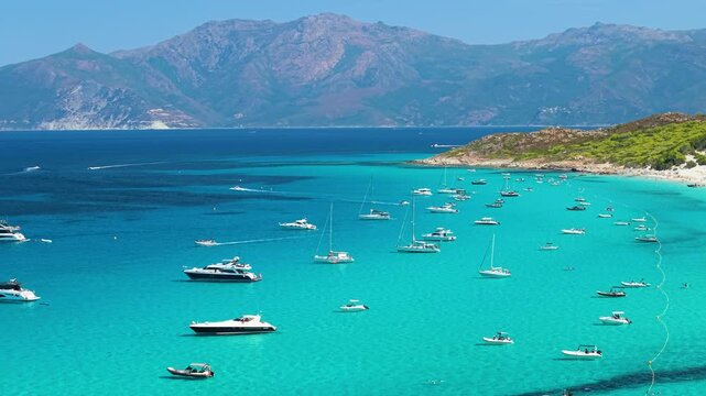 Saleccia beach desert Agriates Corsica tropical turquoise water 70mm cinematic drone footage. Panoramic bay view with anchored yachts sailboats motorboats and high mountain landscape France travel 4k