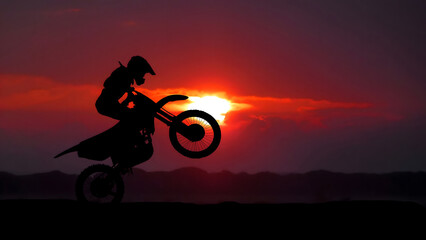 Motocross rider performing a wheelie stunt at sunset, extreme sports action silhouette. © Aswinsasi17