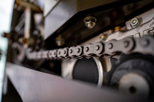 Close up of a heavy duty metal drive chain engaging a toothed sprocket gear wheel in an agricultural machine mechanical transmission system.