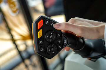 Female hand operating navigation buttons on an ergonomic multifunctional control joystick console inside an agricultural harvester cabin. © Marina