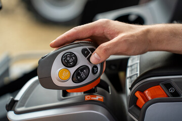 Operator hand holding modern multifunctional control joystick with buttons and emergency stop switch inside agricultural tractor vehicle cabin. © Marina