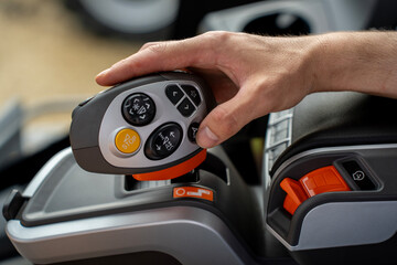 Operator hand holding modern multifunctional control joystick with buttons and emergency stop switch inside agricultural tractor vehicle cabin. © Marina