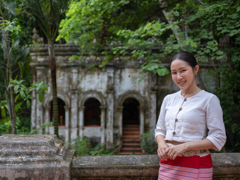 Smiling Asian woman in traditional Thai dress standing in front of ancient temple ruin, Wad Palad Chiangmai Thailand