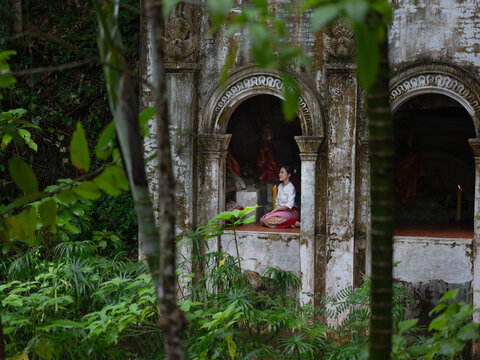 Asian woman in traditional Thai dress framed through circular hole at ancient temple