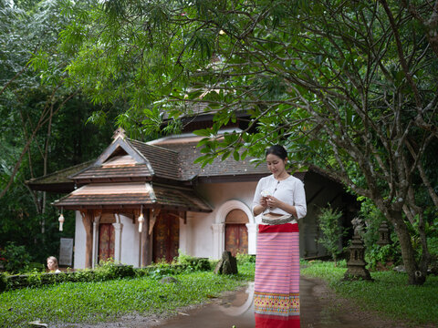 Asian woman in traditional Thai dress standing near ancient temple in forest