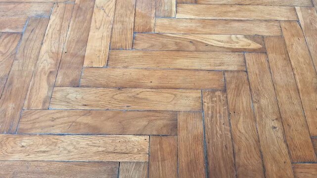 Wooden parquet floor in herringbone pattern with warm brown tones, visible grain, and natural wear marks, showcasing craftsmanship, texture, and decorative interior design detail
