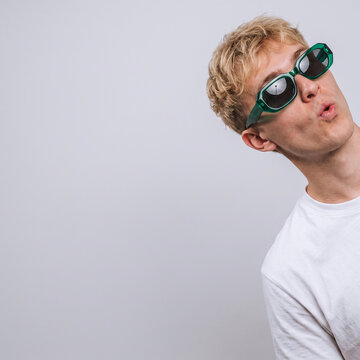 Portrait of a playful young blonde man wearing green sunglasses with puckered lips and copy space