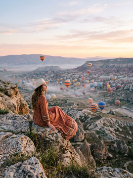 Woman admiring cappadocia landscape with hot air balloons at sunrise in turkey