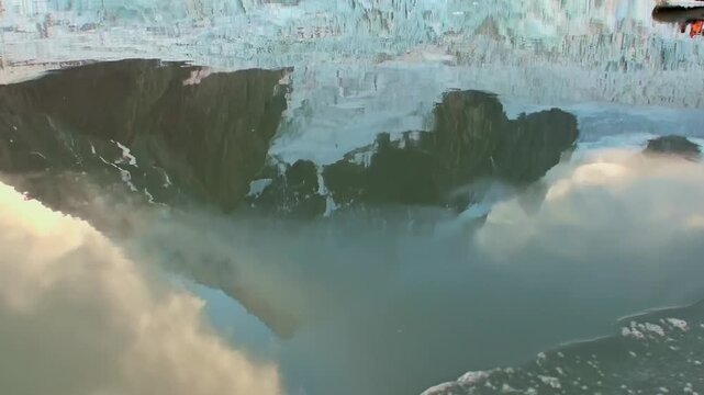 A massive Arctic glacier is reflected across calm cold water, with mirrored ice and the surrounding landscape creating clear depth in the polar scene. Ice texture remains clear.