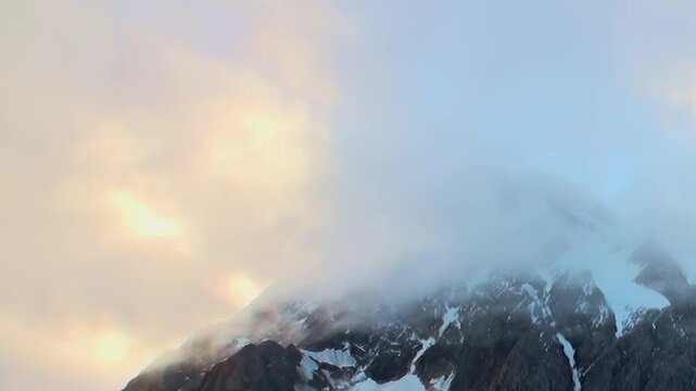 A massive Arctic glacier extends beneath rugged mountain peaks, showing layered ice, frozen terrain, and the scale of the remote polar landscape. Clouds and mist soften distant contours.