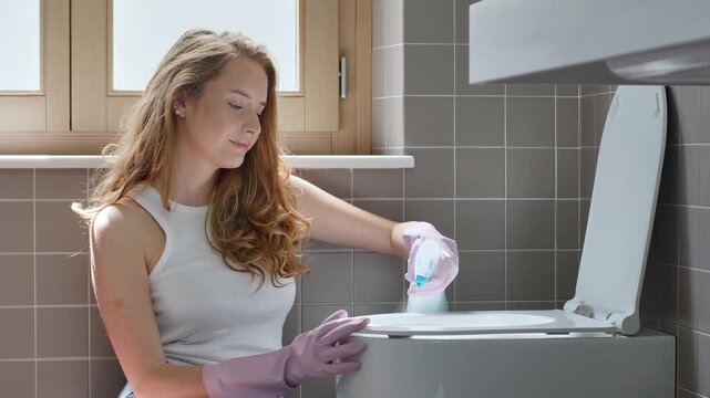 Woman Cleaning and Sanitizing Toilet Seat with Spray Detergent in Bathroom
