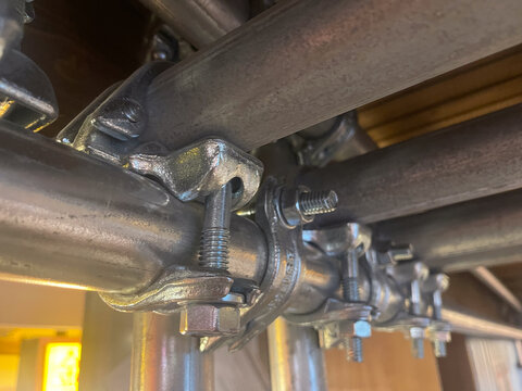 Close up view of heavy duty steel scaffolding couplers and swivel clamps connecting steel pipes together on a construction framework structure.