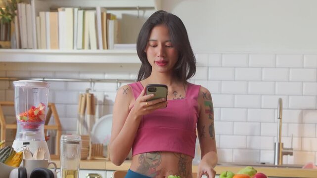 Woman photographing smoothie ingredients with smartphone in kitchen, capturing healthy recipe content for social media, satisfied smile during meal prep documentation concept