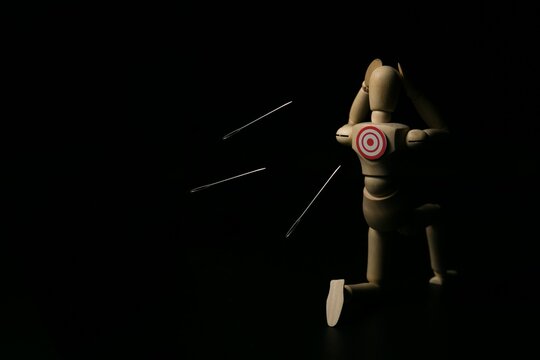 Wooden mannequin with target on back dodging flying needles, concept of stress, pressure, risk, and vulnerability.